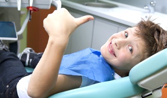 A young patient giving a thumbs-up at their dental appointment.