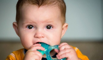 toddler boy chewing on blue teething ring 