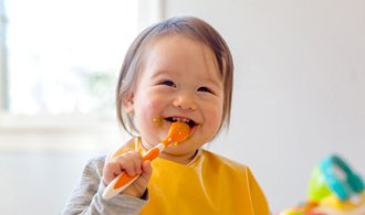 toddler girl smiling while eating a meal 
