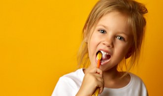 little girl brushing her teeth against yellow background 