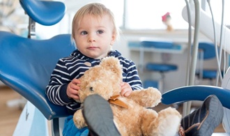toddler holding teddy bear in dental chair 