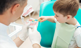 Child in dental chair practicing tooth brushing on model