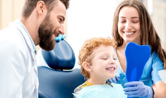 little boy looking at his teeth in mirror in dental chair 