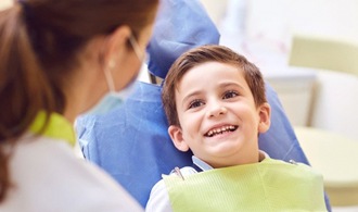 little boy sitting in dental chair and smiling at dentist 