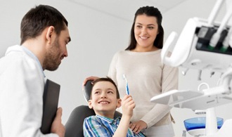 little boy holding up toothbrush in dental chair 