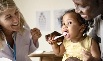 pediatric dentist showing toddler girl how to brush her teeth 