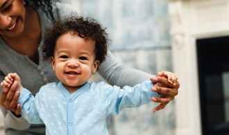 mother helping toddler boy learn to walk 