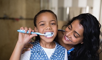 A girl brushing her teeth while her mother watches