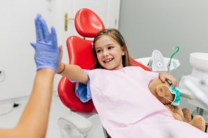 Smiling girl in examination chair high-fiving her Hillsborough pediatric dentist