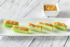 Cuts of celery topped with peanut butter on a white plate sitting on a white wooden table