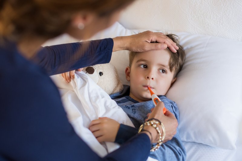 A child having their temperature taken while their mother worries about their oral health