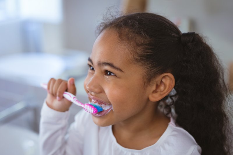 A smiling little girl brushing her teeth